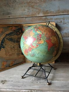 an old globe sits on a stand in front of two antique maps, one is green and the other is red