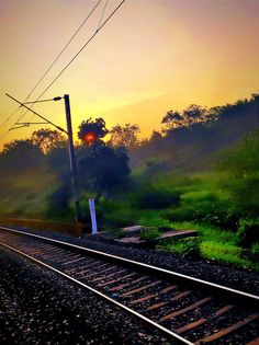 a train track with the sun setting in the background and trees to the side,