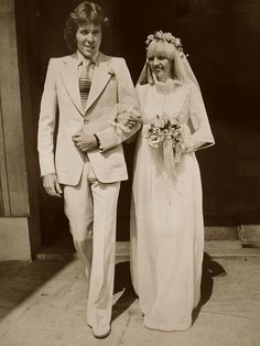 an old black and white photo of a man and woman in wedding attire standing next to each other