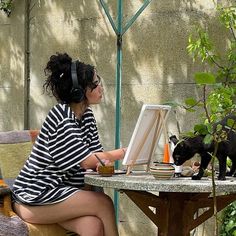 a woman sitting at a table with a cat on her lap and an easel in front of her