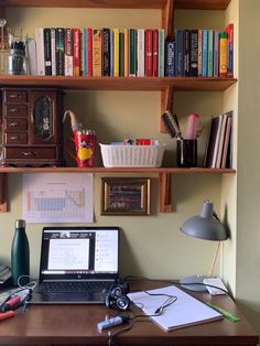 a laptop computer sitting on top of a wooden desk next to a bookshelf