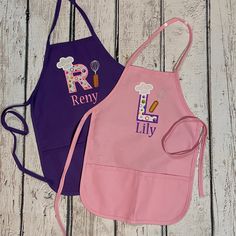 two children's aprons with personalized designs on them sitting on a wooden surface