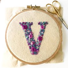 the letter v is made up of flowers and has been stitched into an embroidery hoop