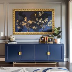 a painting hangs on the wall next to a blue cabinet with gold handles and drawers