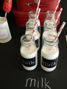 four glass jars filled with milk sitting on top of a table next to a red suitcase