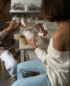 two women sitting at a table with bowls and paintbrushes in their hands,