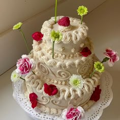 a three tiered white cake with flowers on the top and bottom, sitting on a lace doily