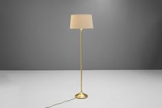 a floor lamp with a white shade on the top and a gold chain around it