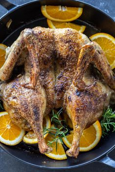 a whole chicken in a skillet with oranges and rosemary