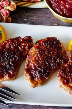 three pieces of meat covered in ketchup on a plate next to orange slices