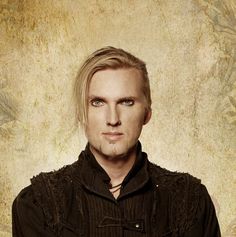 a man with blonde hair and blue eyes wearing a black shirt looking at the camera