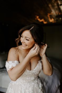 a woman in a wedding dress smiles as she adjusts her hair