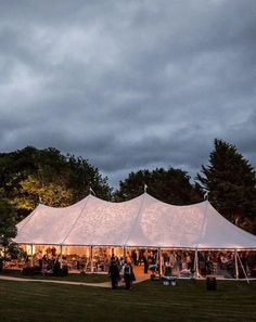 a group of people standing in front of a white tent at night with dark clouds overhead