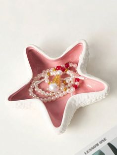 a pink starfish shaped dish with pearls and a ring on it's side