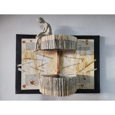 a sculpture made out of old book pages sitting on top of a wooden table next to a black frame