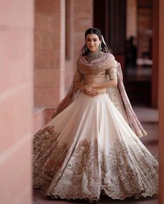 a woman in a white and gold lehenga is posing for the camera with her hands on her hips