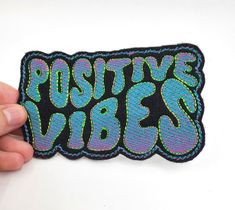 a person holding up a patch with the words positive vibes in neon blue and green