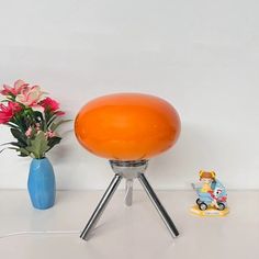 an orange lamp sitting on top of a table next to a blue vase with flowers