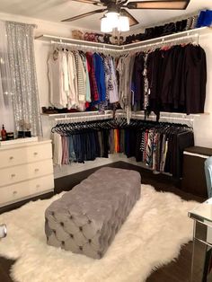 an organized closet with white fur rugs and clothes on hangers, including a bench