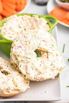 two bagels with cream cheese and carrots in the background on a white plate