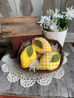 three yellow and white decorated eggs in a basket on a table next to some daisies