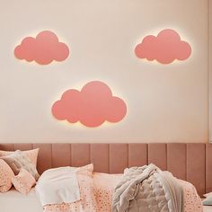 a bed with pink clouds on the wall above it, and pillows in front of it