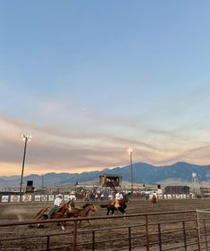 people riding horses in an arena with mountains in the background