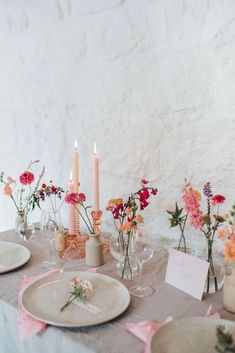 the table is set with plates, candles and flowers in vases on top of it