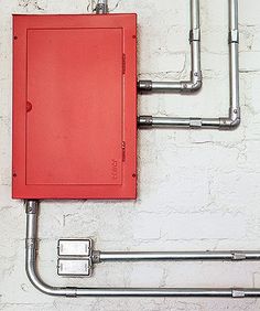 a red box is attached to the side of a white brick wall with metal piping