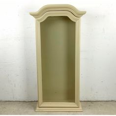 a tall white shelf with a mirror in it's corner on the floor next to a wall