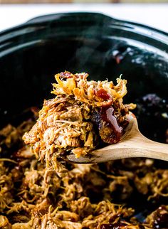 a wooden spoon is full of shredded meat and bbq sauce in a crock pot