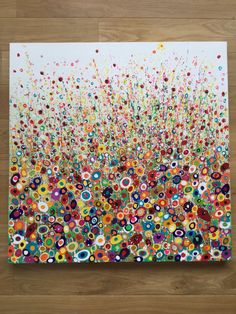 an abstract painting with colorful circles and dots on white paper, sitting on a wooden floor