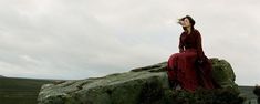 a woman in a red dress sitting on top of a large rock with her eyes closed