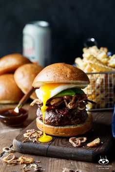 a hamburger with an egg on top and fries in the background