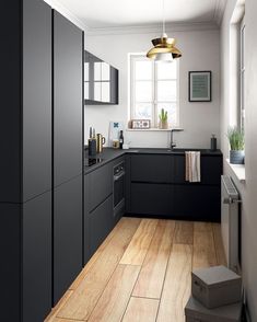 a kitchen with black cabinets and white walls, wood floors and a gold pendant light hanging over the sink