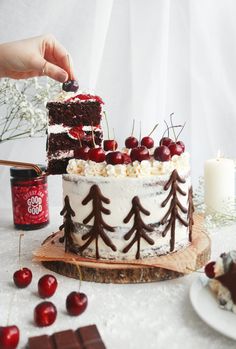 someone is decorating a cake with cherries and chocolate on the table next to it