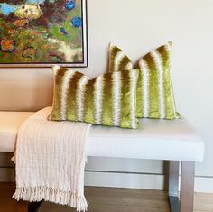 two green and white pillows sitting on top of a bench next to a framed painting