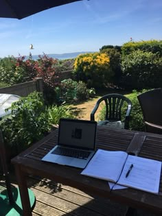 an open laptop computer sitting on top of a wooden table next to a garden filled with flowers