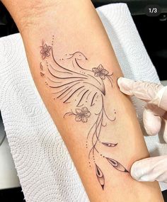 a woman is getting her tattoo done on her arm and the bird has flowers in its beak