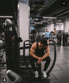 a man squatting on a bench in a gym with other people working out behind him