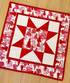 a red and white quilted table topper on a wooden floor with pine trees in the background