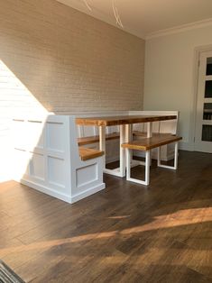 an empty room with wooden flooring and white benches on the side wall, in front of a brick wall