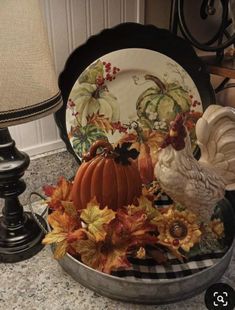 a metal bowl filled with pumpkins, leaves and a chicken figurine on top of a table