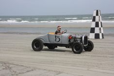 a man driving an antique race car on the beach