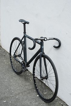 a black bicycle leaning against a white wall