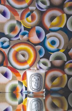 a white candle sitting on top of a table next to a wall covered in colorful circles