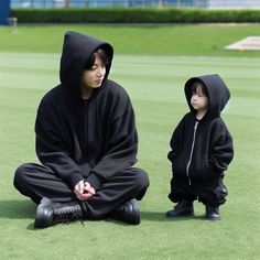 a young boy sitting on the ground next to an adult in a black hoodie