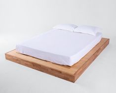 a bed that is made up with white sheets and pillows on top of it, sitting on a wooden platform