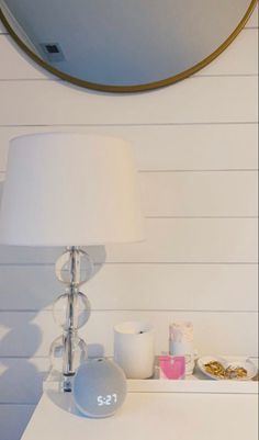 a table with a lamp, mirror and other items on it in front of a white wall