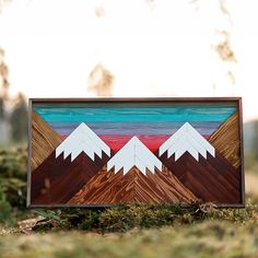 a painting with mountains in the background and grass on the ground next to it that is made out of wood